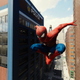 Spidey leaps down a street in broad daylight, the sky reflected in the windows of a nearby police station.